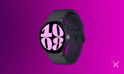 A black smartwatch displaying a large digital clock reading "10:08" in white on a pink background, with a purple backdrop.